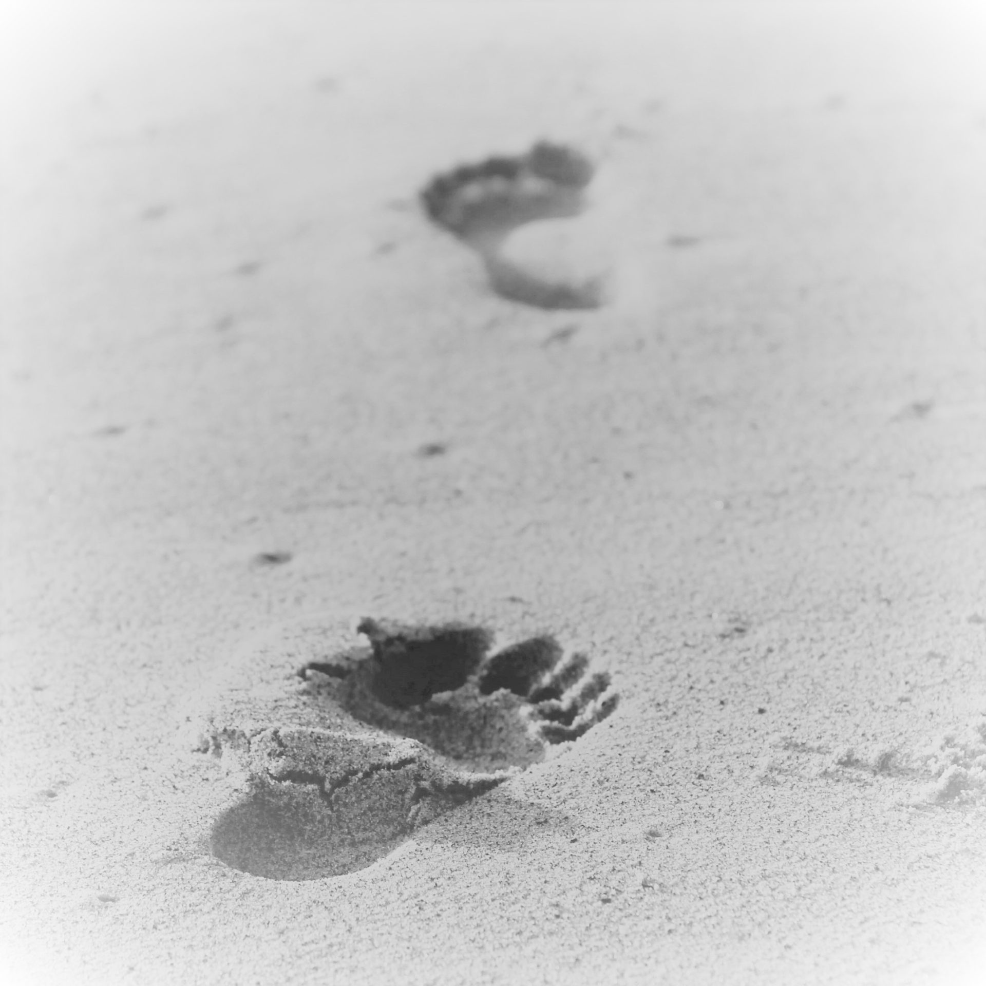 Zwartwitte afbeelding van twee voetafdrukken in zand (op een strand).